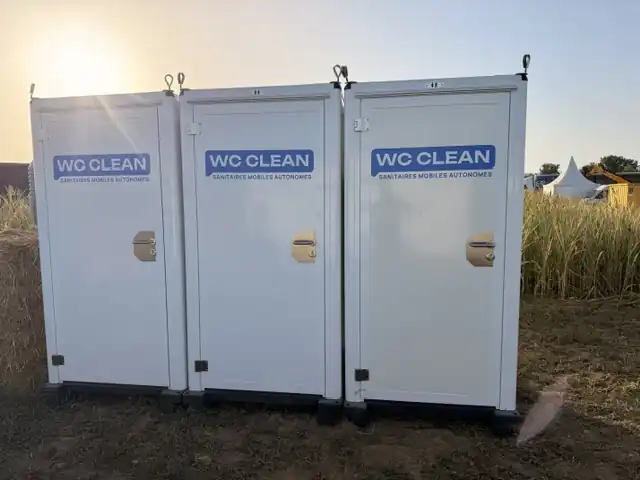 Trois cabines WC Clean alignées en plein air, au soleil couchant