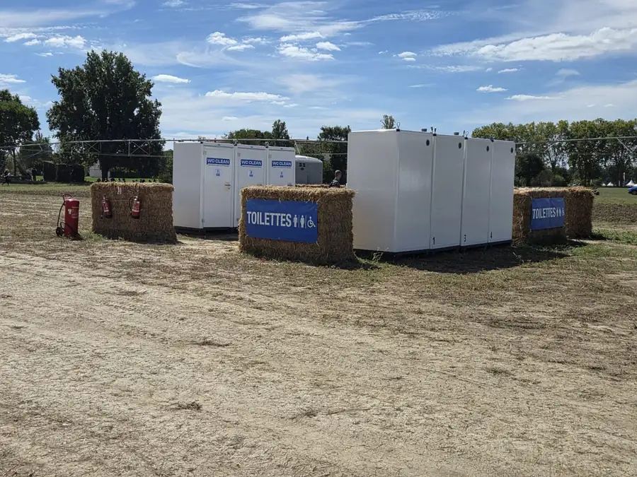 Cabines WC Clean et cabine PMR alignées sur un événement en plein air, signalées par des panneaux Toilettes